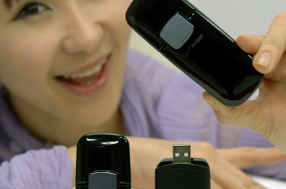 A model posing with a closed LG Verizon Wireless LTE USB Modem while two stand up perfectly on the table, one with the lid open and the other with the lid closed