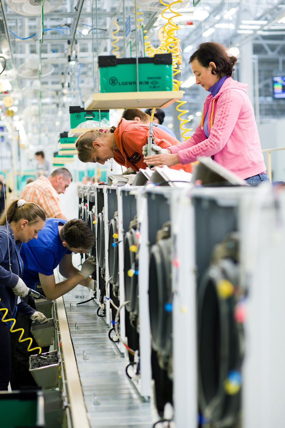 Many factory staff members assemble washing machines at an appliance manufacturing plant in Poland