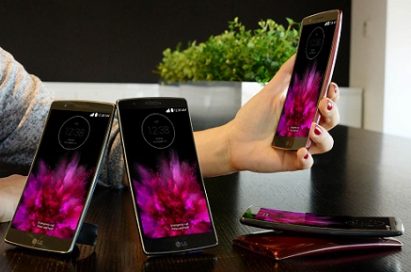 A hand of a female model holds up an LG G Flex2 behind another four G Flex2 phones positioned on the table.