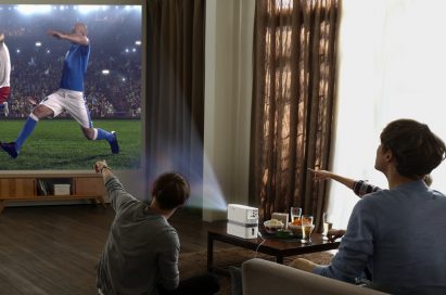 Three people watch a soccer game projected on the wall by the LG Probeam Laser Projector (model HF80J)