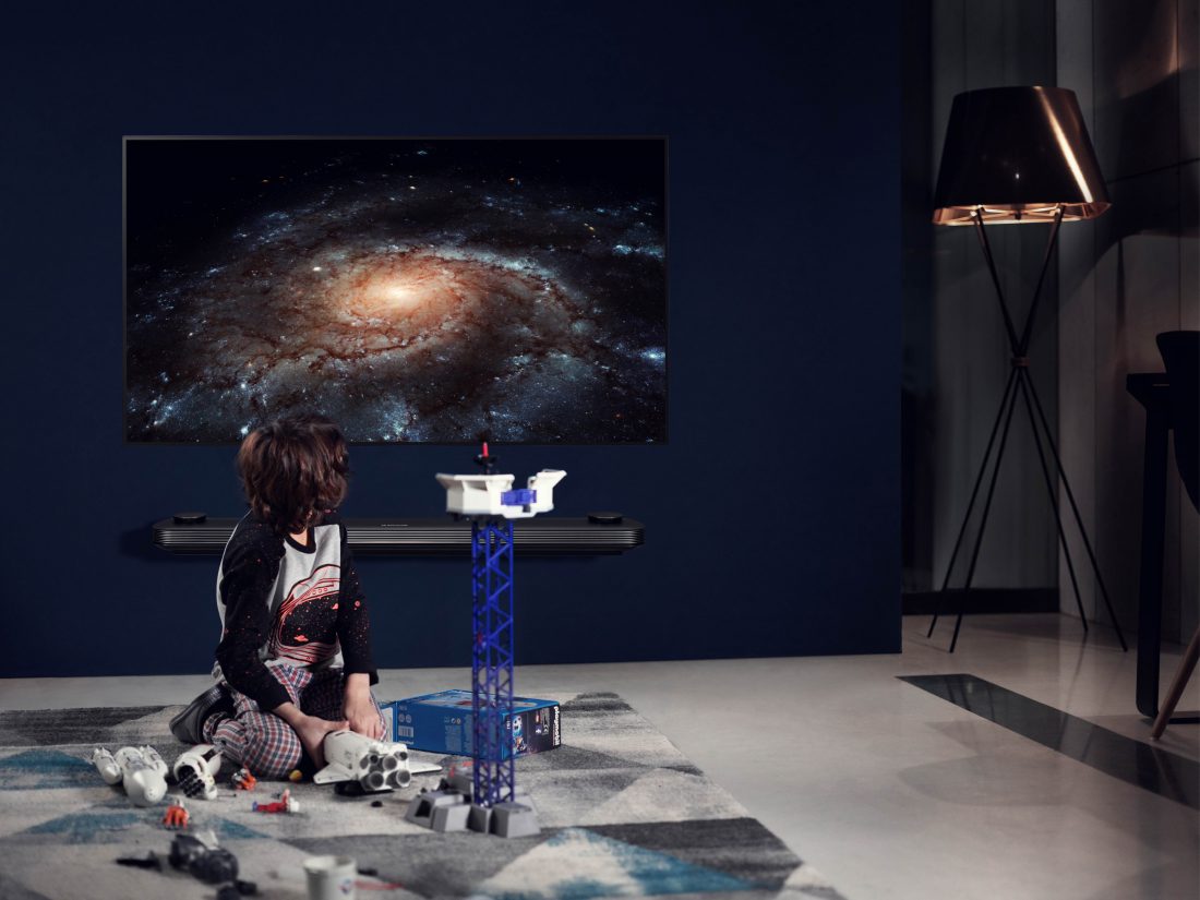 A small boy plays with space toys while the LG SIGNATURE OLED TV W is displayed on the wall with a picture of a galaxy on the screen.