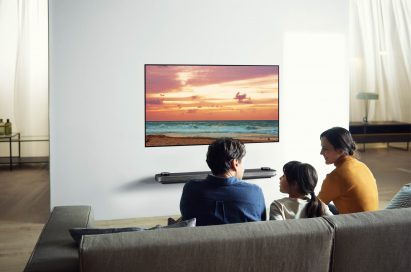 Another view of a family sitting in their living room looking at the LG SIGNATURE OLED TV W (model 7) which is mounted seamlessly on the wall