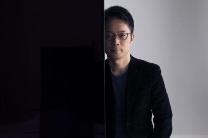 Tokujin Yoshioka stands behind one of LG screens making up his art installation wall looking into the camera.