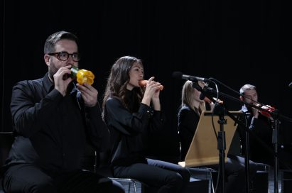 A close-up of four members of the London Vegetable Orchestra performing with their makeshift vegetable instruments.