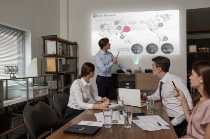 People in a business meeting watch a presentation that is being projected on the wall by the LG ProBeam Projector HF85J.