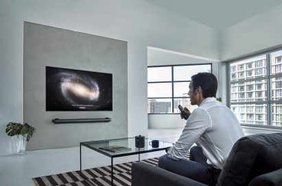 A man watching his LG OLED TV with a remote in one hand at his home