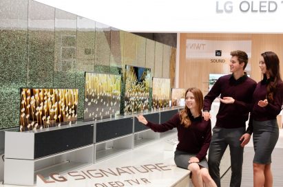 Three people are looking at LG OLED TV R on display at LG’s CES 2019 booth