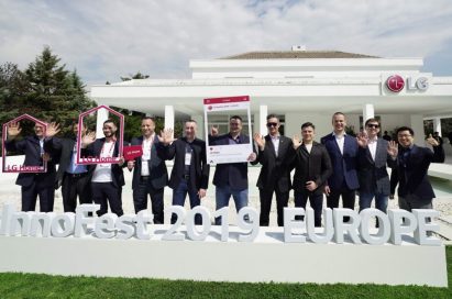 Attendees of LG InnoFest 2019 Europe wave their hands towards the camera in front of LG Home Madrid.